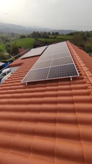 Placas solares sobre cubierta de teja curva con el valle asturiano al fondo