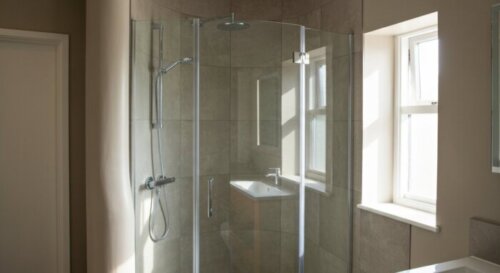 A detailed, photorealistic image of a modern bathroom with a curved wall, showing a custom-made curved glass shower enclosure installed seamlessly against the irregular surface. The shower has chrome