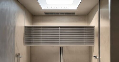 Photorealistic close-up of a modern walk-in shower enclosure with an integrated ventilation system in a small bathroom. The extractor grille is visible on the top frame, with a sleek glass panel and m