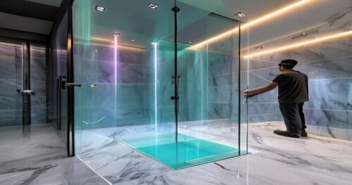 A modern bathroom with a glass shower enclosure featuring integrated hydrotherapy jets and chromatic LED lights. The walls and floor are covered in large-format porcelain tiles with a marble look. The