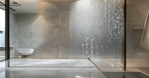 Photorealistic close-up of a glass shower screen with a water droplet sliding off, showing the photocatalytic self-cleaning effect, installed on a microcement wall and liquid porcelain floor. The scen