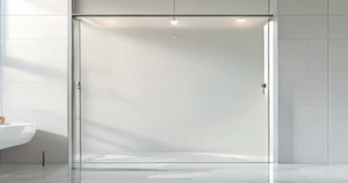 Photorealistic close-up of a frameless glass shower door with invisible hinges installed on a white plasterboard wall, overlapping a seamless liquid porcelain floor. The hinge is embedded in the wall,