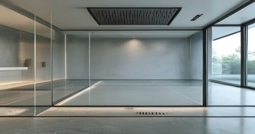 Photorealistic close-up of a frameless glass shower enclosure installed on a microcement floor with visible underfloor heating pipes marked on the floor plan. The image shows a silicone joint between