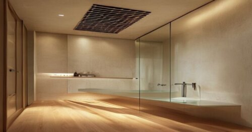 A photorealistic image of a modern bathroom with a glass shower enclosure installed on a floating wood floor. The shower base has a low aluminum profile sealing the joint between the glass and the woo