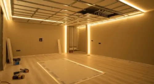 A modern bathroom with a suspended plaster ceiling featuring integrated LED strip lighting around the perimeter, warm light, vinyl flooring, and radiant heating visible through a cutaway. The ceiling