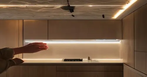 Close-up photo of hands installing a sleek LED strip under a modern kitchen cabinet, with a plasterboard ceiling and hidden cables, realistic lighting, no text.