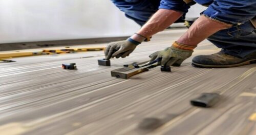 A professional builder measuring and snapping SPC click vinyl planks over a radiant floor, using tapping block and pull bar, leaving expansion gaps at the wall with spacers, tools spread around, reali
