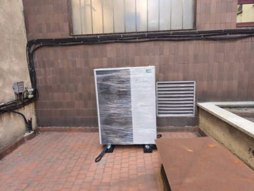 Unidad exterior de aerotermia instalada en el patio interior de un edificio, sobre soportes antivibratorios
