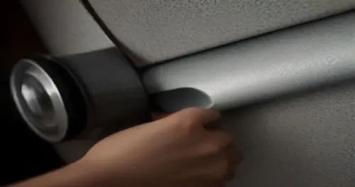 Close-up of a person's hands wrapping a plumbing pipe inside a drywall partition with acoustic mineral wool and aluminum tape, tools visible, realistic lighting, construction site background.