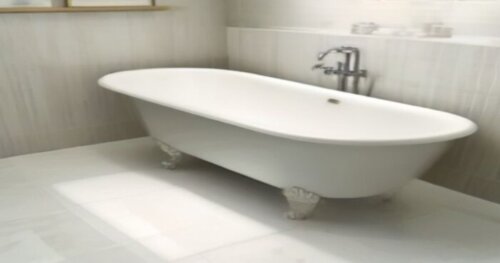 Photorealistic image of a freestanding white bathtub placed on large-format porcelain tile floor with subtle underfloor heating pipes visible as a thermal pattern. A caulking gun with polyurethane adh